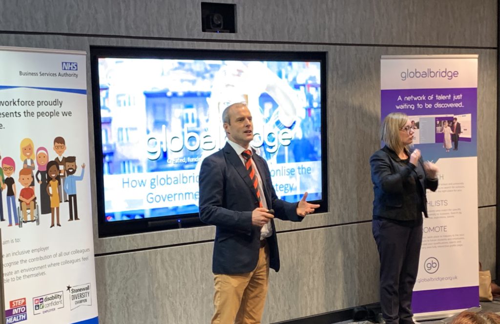 Man standing and giving a presentation in front of a large screen.